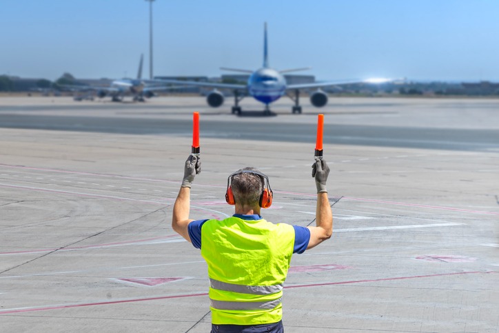 a man in a yellow vest and safety vest holding a red light airplane marshall
