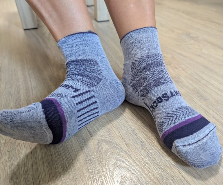 Samantha's feet wearing gray moisture-wicking Wrightsocks performance crew socks on a wooden floor.