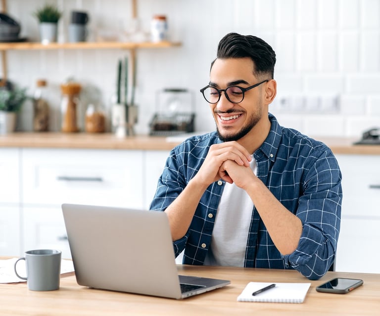 Man sitting at kitchen table, smiling happily towards his laptop