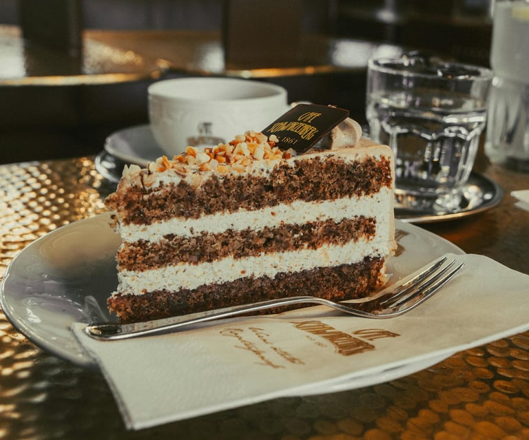 A slice of layered hazelnut cream cake topped with crushed nuts at a cafe.