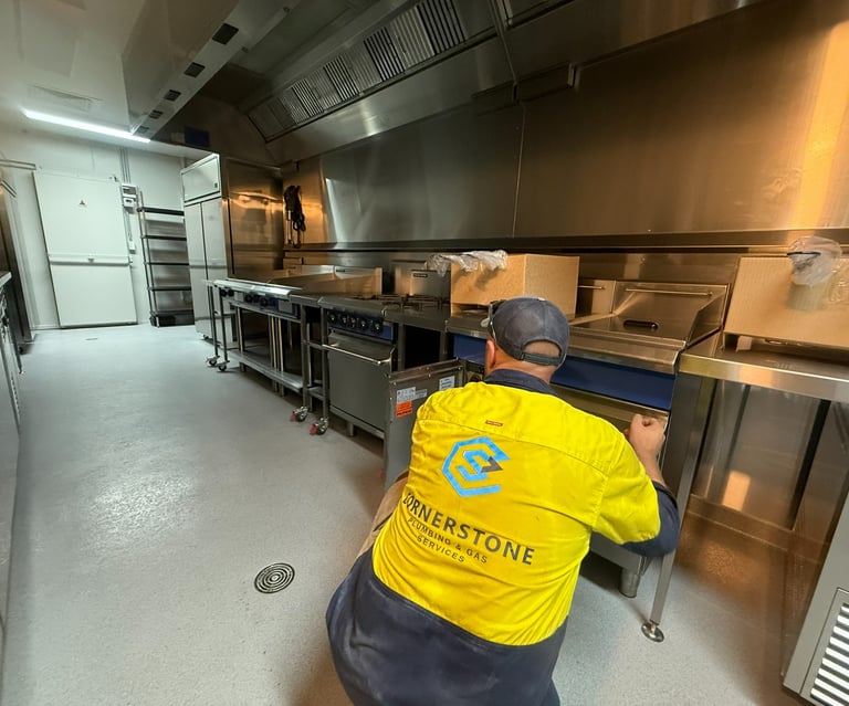 Professional plumber installing commercial kitchen equipment and gas appliances in a restaurant.