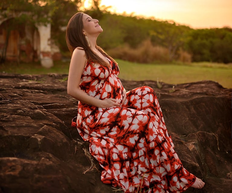 Mulher de vestido vermelho longo sentada em meio a natureza com paisagem