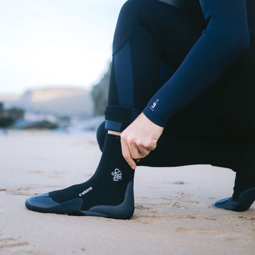 A man pulling on a wetsuit boot at the beach