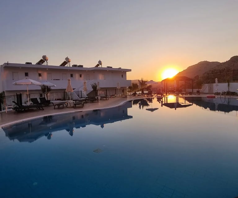 Luxury resort swimming pool reflecting a golden sunset over Mediterranean hills and white villas.