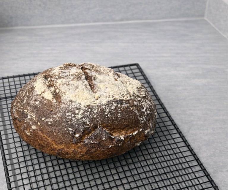 Freshly baked gluten-free artisan bread cooling on a black wire rack atop a grey countertop.