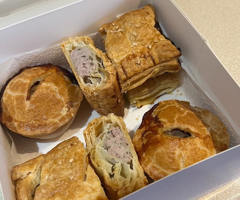 Golden brown gluten-free sausage rolls and pork pies in a white bakery takeaway box.