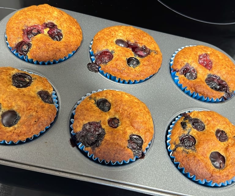 Freshly baked gluten-free blueberry muffins in blue paper liners cooling in a metal baking pan.