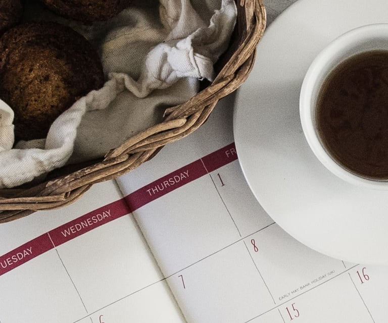 Calendar with cup of coffee and muffins on white table