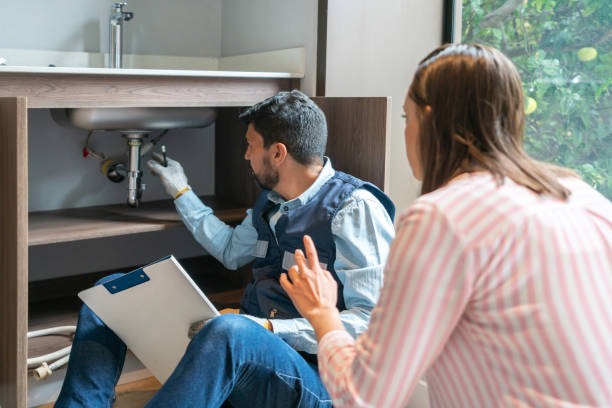 plumber pointing under a sink and explaining things to a woman