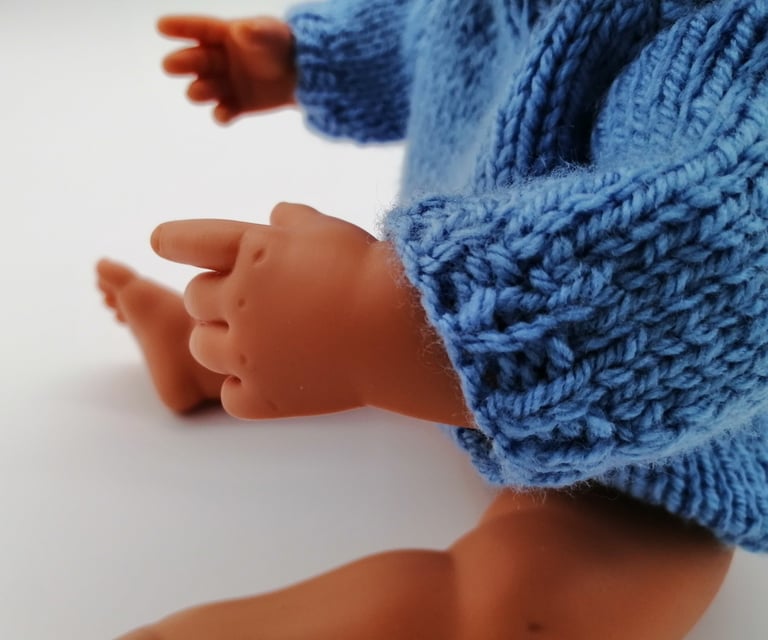 Miniland doll sitting wearing blue knitted jumper