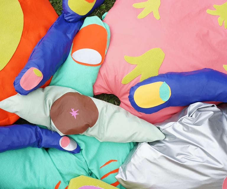 Soft sculptures of fingers, eyes, a tongue and a neuron displayed on grass on a hot sunny day.