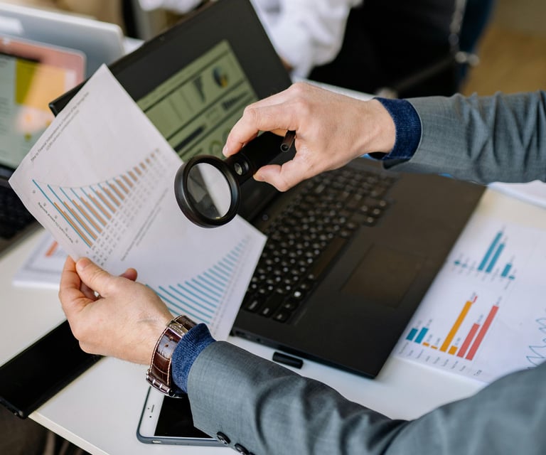 A businessman using a magnifying glass to analyze financial growth charts and data reports on his desk.