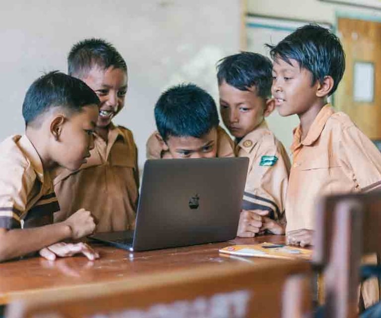 a group of children in school uniforms looking at a laptop