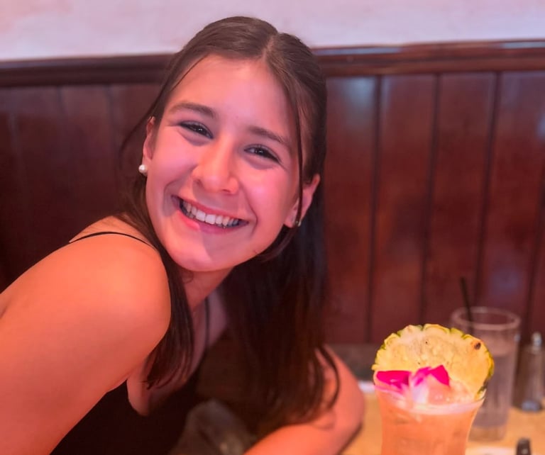 A girl smiling while at a table drinking a drink