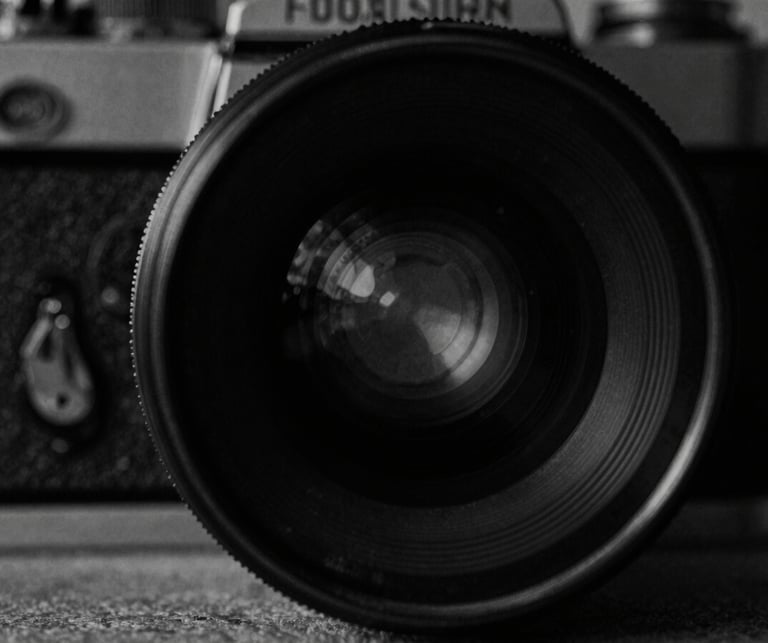Close-up of a vintage film camera lens, high-contrast monochrome, moody low-key lighting, 35mm grain, cinematic film photography