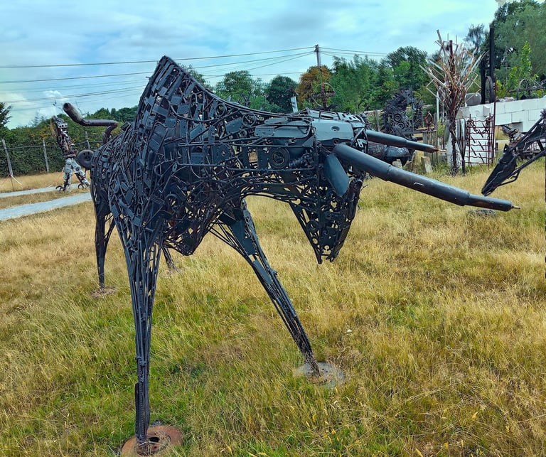 A metal bull sculpture made of recycled scrap metal parts standing in a grassy field.