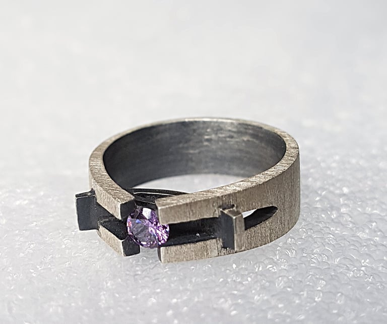 a ring with a purple stone ring on top of a white surface