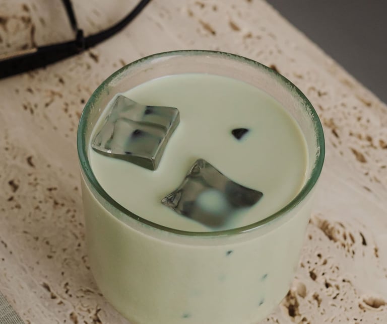 Iced matcha green tea latte with large ice cubes in a glass on a travertine stone surface.
