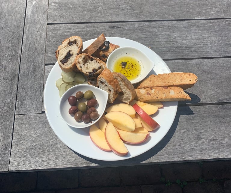 A snack plate of apples, bread, olives, pickles, and biscotti 