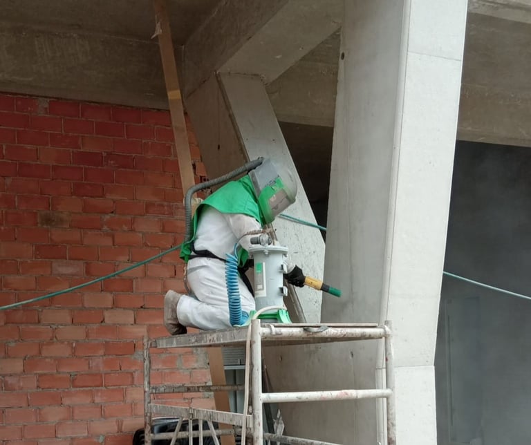 Técnico especialista en el chorreo de arena chorreando hormigón en un andamio