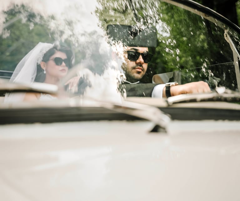 Bride and groom wearing sunglasses driving a classic car, captured by Fred Art Studio.
