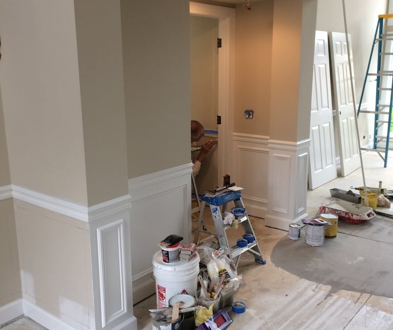 Professional interior home painting project featuring white wainscoting and tan walls with painting supplies.
