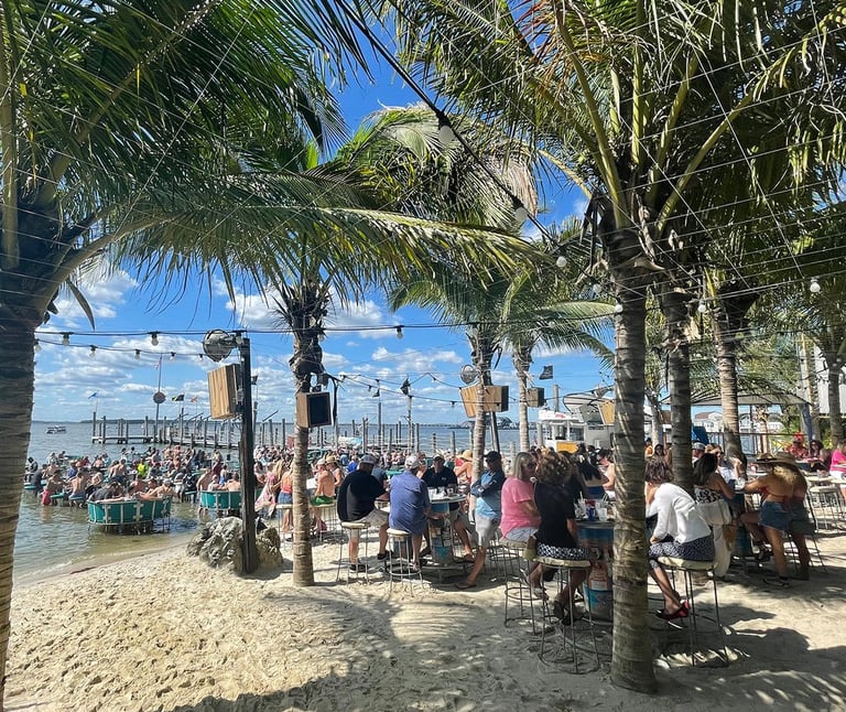 a beach with people sitting at tables and palm trees
