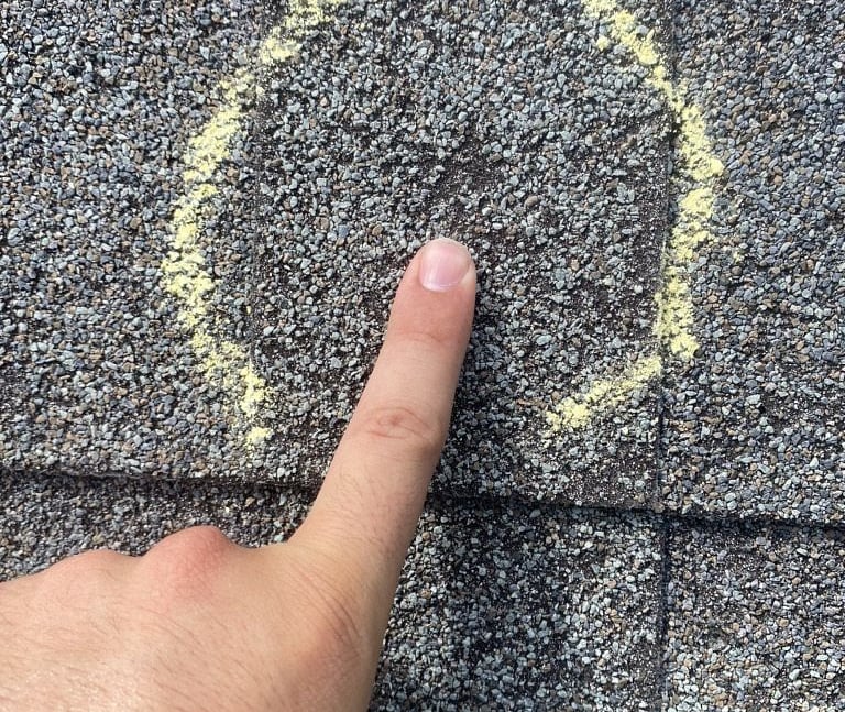Roof technician points out hail damage to shingle so that insurance company can note damage to roof