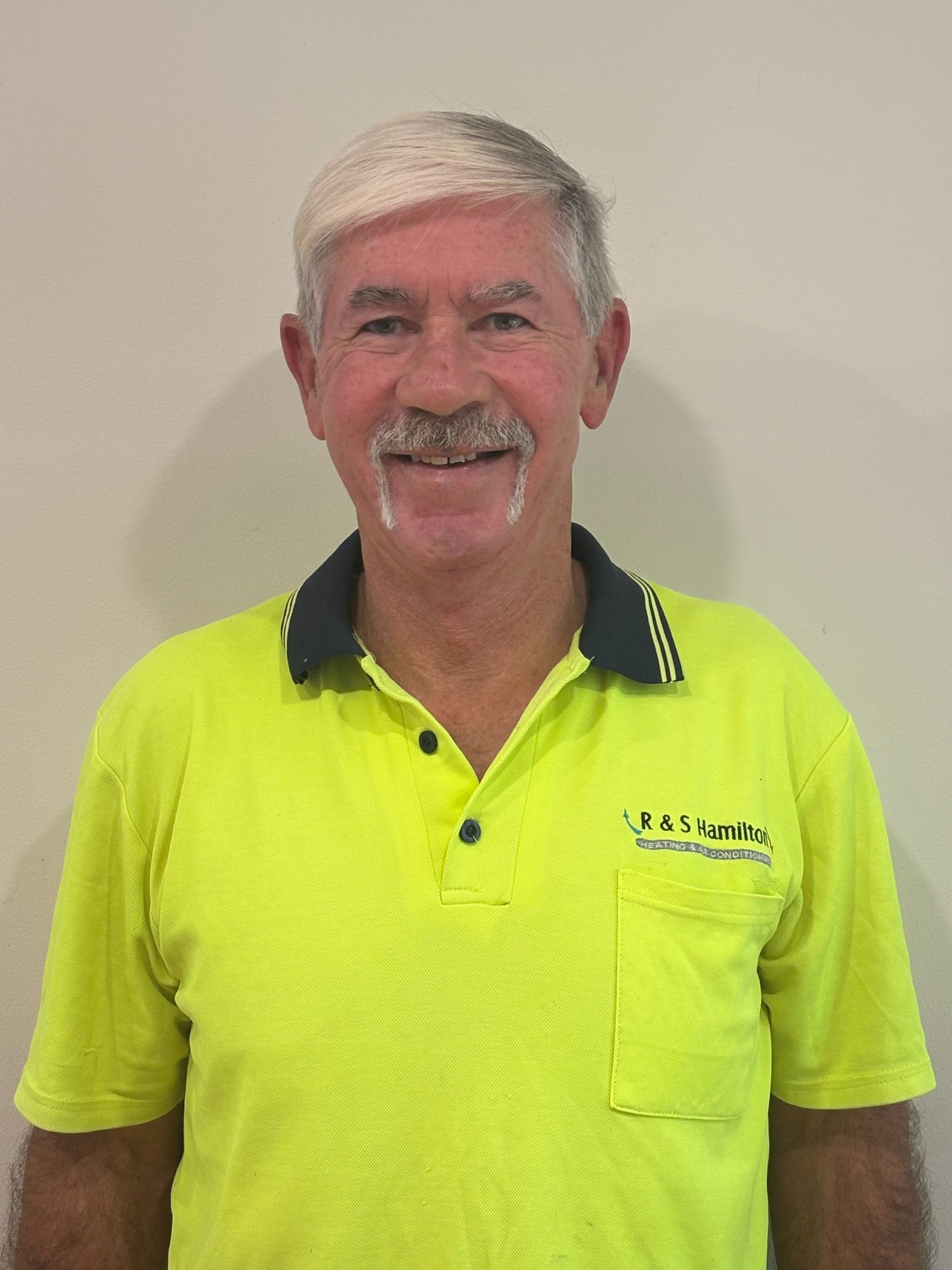 A smiling heating and air conditioning technician from R&S Hamilton wearing a yellow uniform.