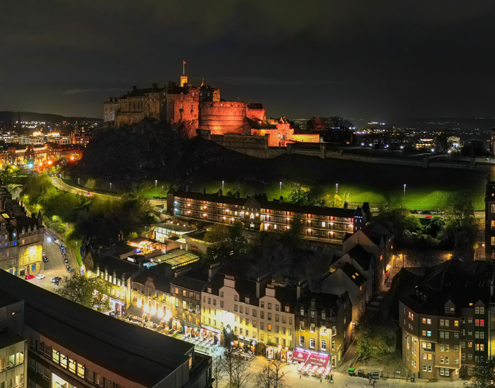 Edinburgh Castle floodlit at night above the Grassmarket with city lights below