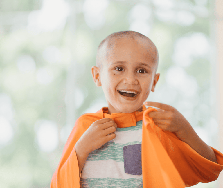Criança que está passando pelo tratamento contra o câncer brincando com uma capa laranja