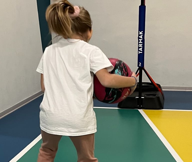 Bambina che gioca con un pallone su un campo multisport nella palestra Move 2 Grow a Milano, utilizzando cerchi colorati
