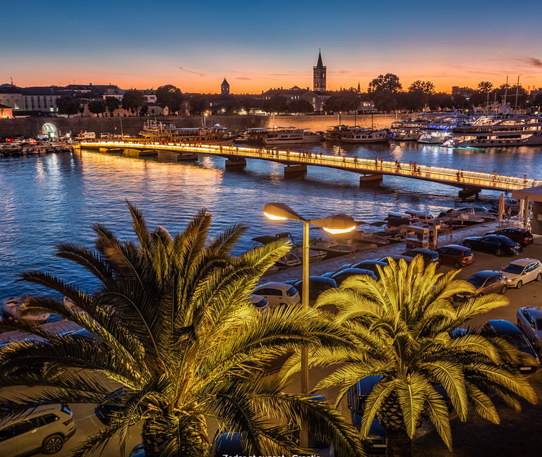 Sunset view of Zadar city bridge and harbor with palm trees and yachts in Croatia.