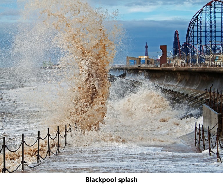a large wave crashes over a pier with a roller coaster and blackpool tower