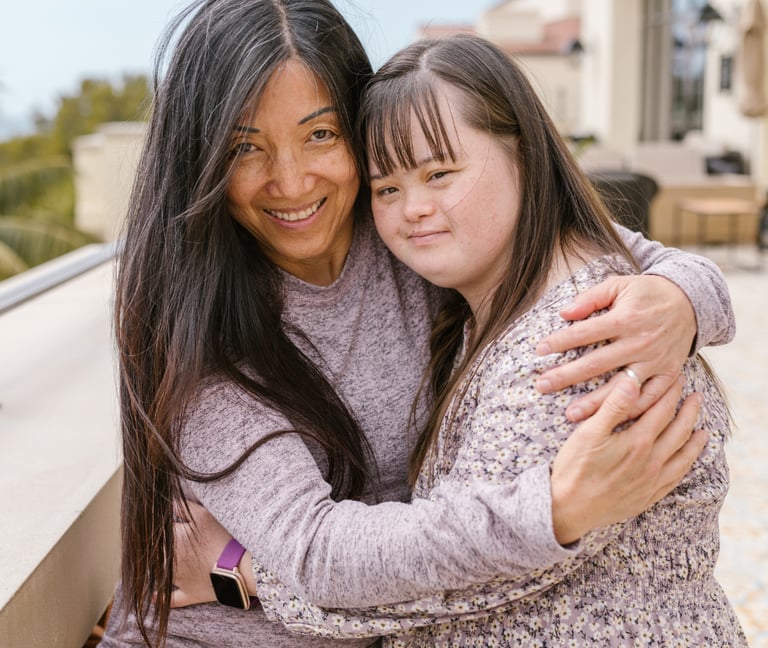 une femme et une jeune fille trisomique se serrent dans les bras et sourient.