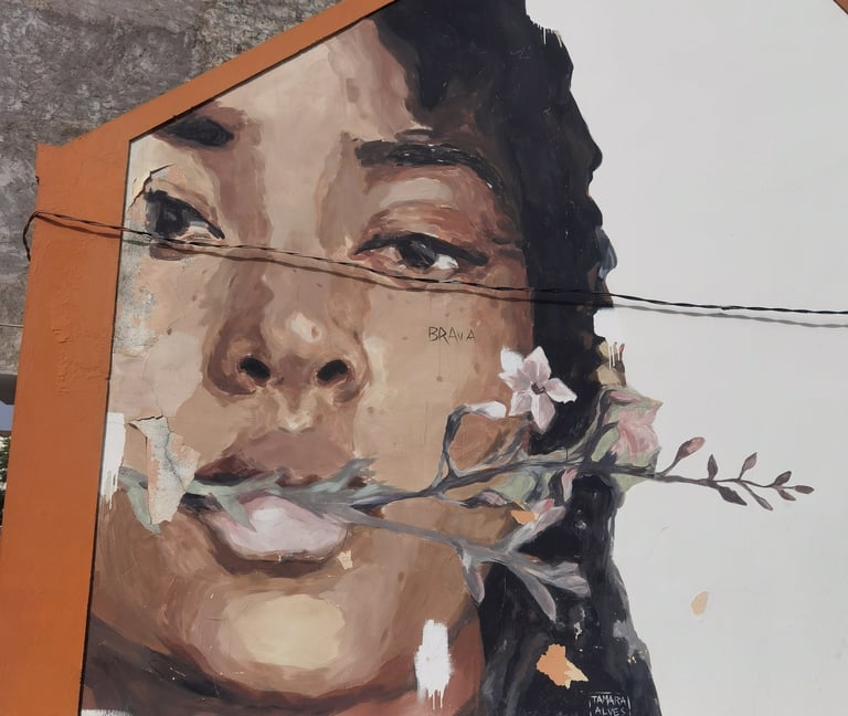 Mural painting of a woman's face with a flower branch in her mouth on a white building wall.