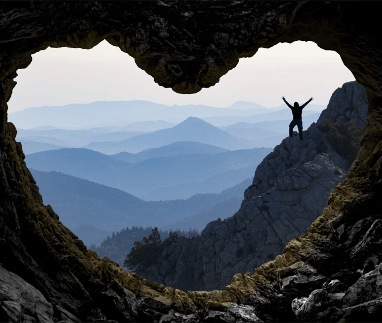 a person standing on a mountain top with a heart shaped hole in the middle of