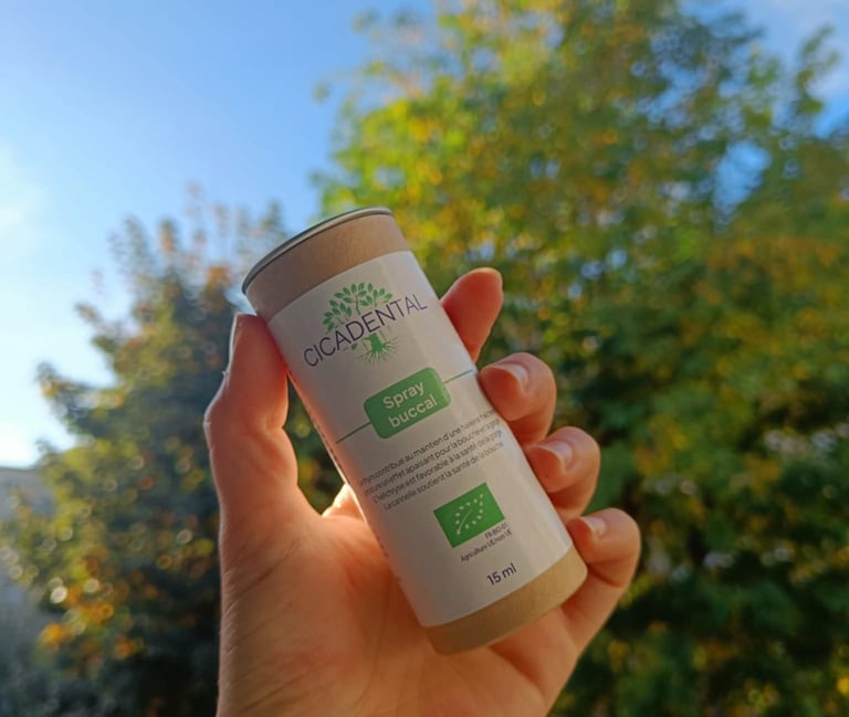 Hand holding a bottle of Cicadental organic buccal spray against a natural green tree background.