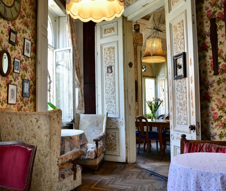 Vintage tea room with floral wallpaper, antique wingback chairs, and cozy tables in a classic European cafe.