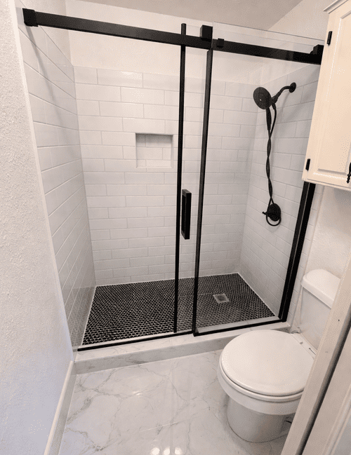 Modern bathroom renovation featuring a walk-in shower with black frame glass doors and white subway tile.