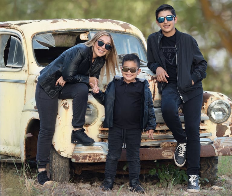 mamá, hijo pequeño e hijo mayor posados cerca de un coche antiguo en el bosque