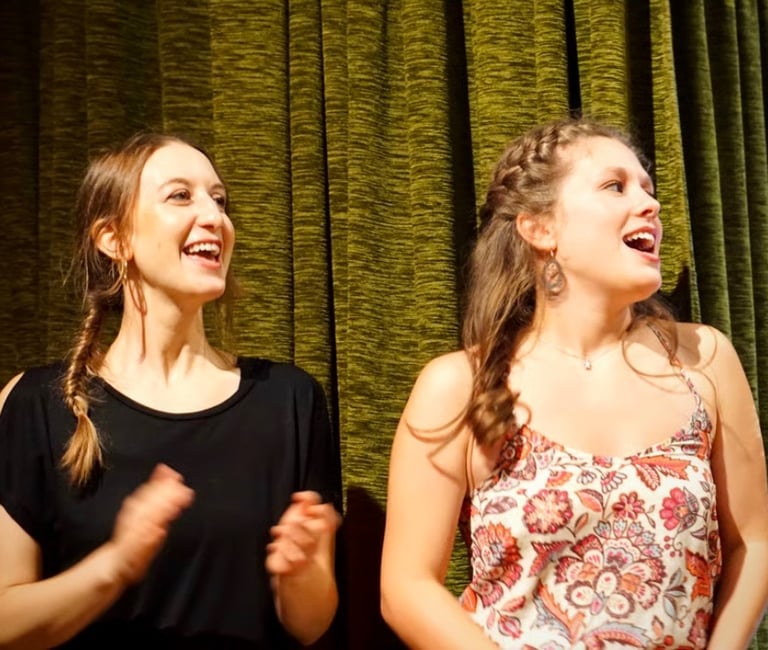 zwei junge Frauen auf der Bühne, die mit Freude singen