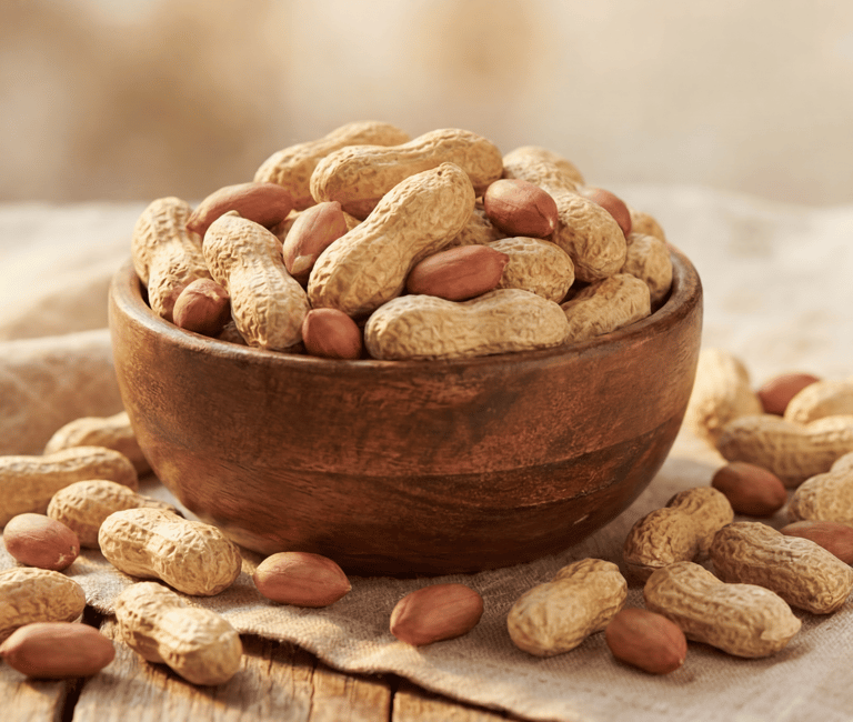 A wooden bowl filled with whole roasted peanuts in shells and shelled red skin peanuts on a rustic cloth.