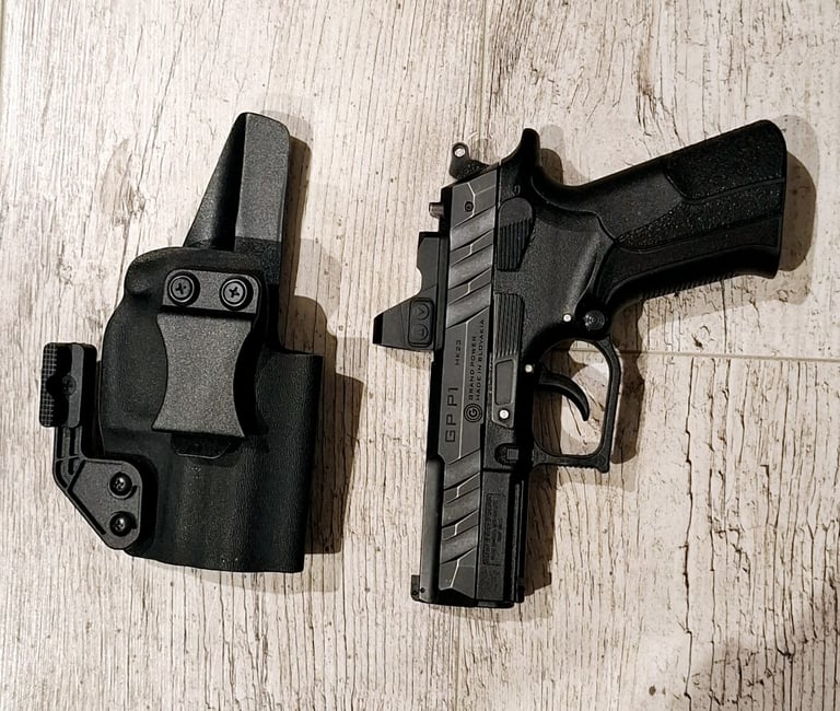Grand Power P1 MK23 pistol with red dot optic next to a black Kydex IWB holster on wood floor.