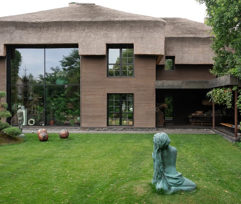 Nowoczesny dom jednorodzinny z dużymi przeszkleniami i strzechą, ogród i rzeźba na trawniku