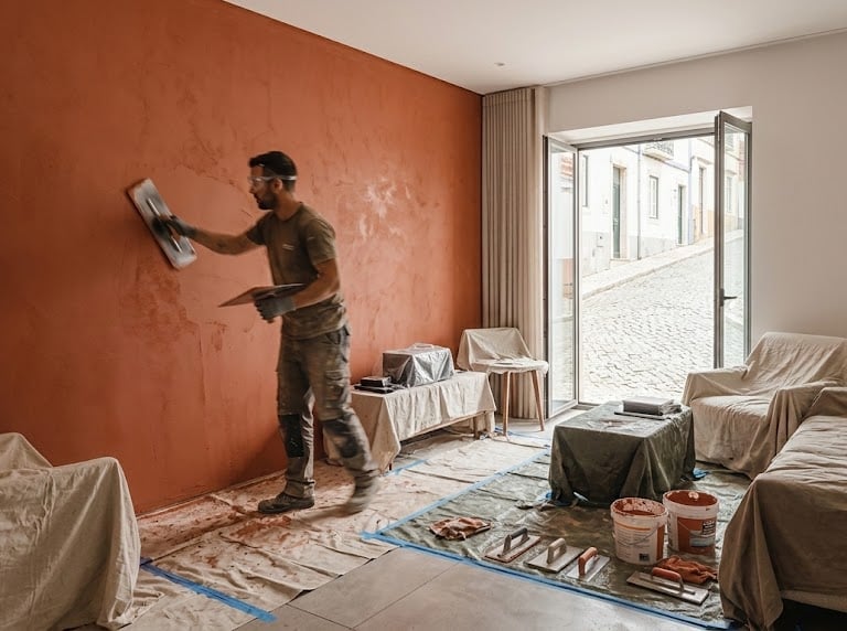 Professional contractor applying decorative plaster to a terracotta accent wall during a home renovation.