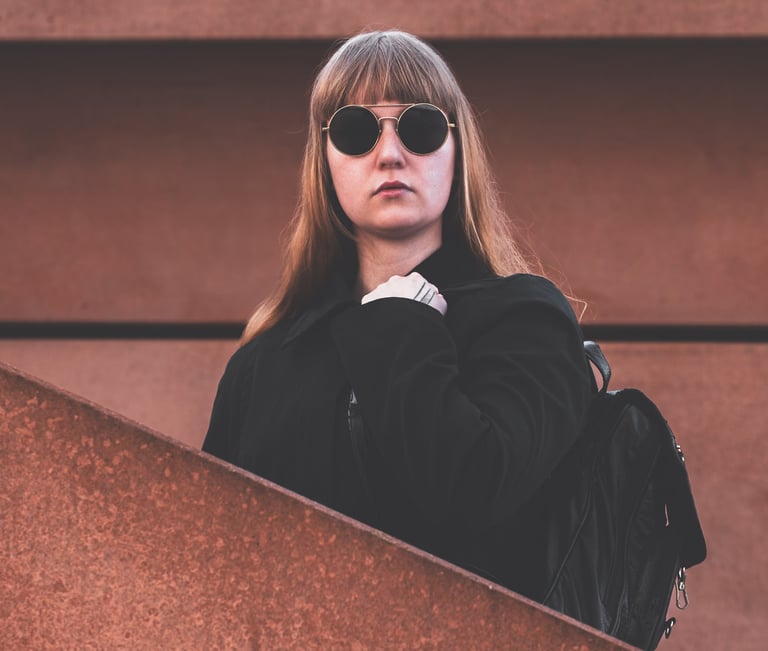 a woman in sunglasses and a black jacket standing in between a wall and a staircase