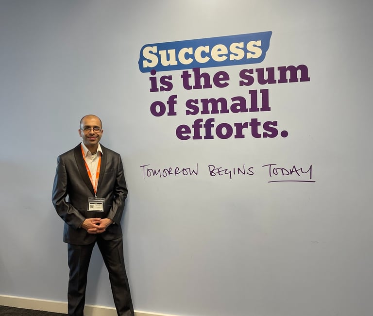 A businessman in a suit stands by an office wall with a motivational success quote.