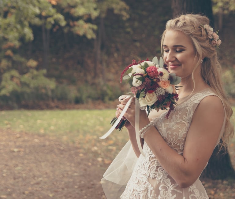 Nuotaka švelniai uodžia savo gėlių puokštę, ant jos rankų perlų apyrankė, romantiška šukuosena