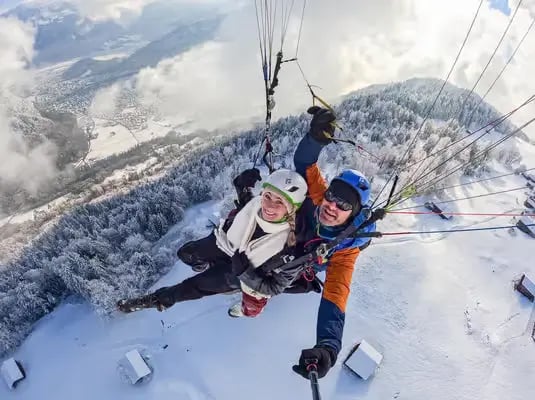 Happy couple taking a selfie while tandem paragliding over snowy Interlaken trees